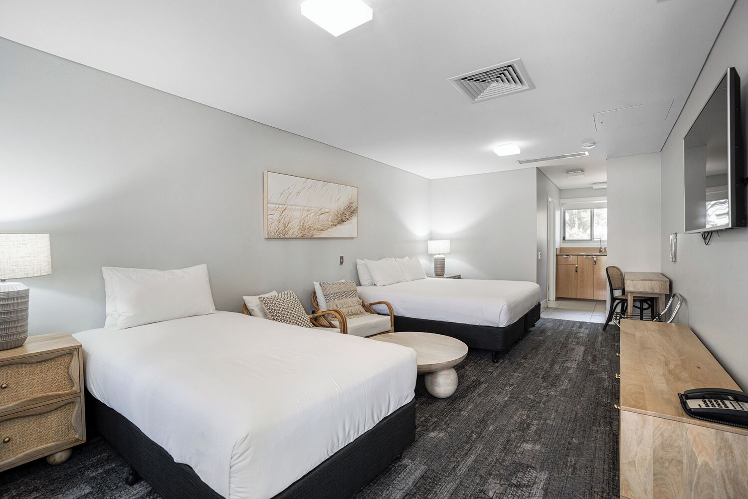 A hotel room with two beds, a desk, a chair, a round table, and a TV mounted on the wall.
