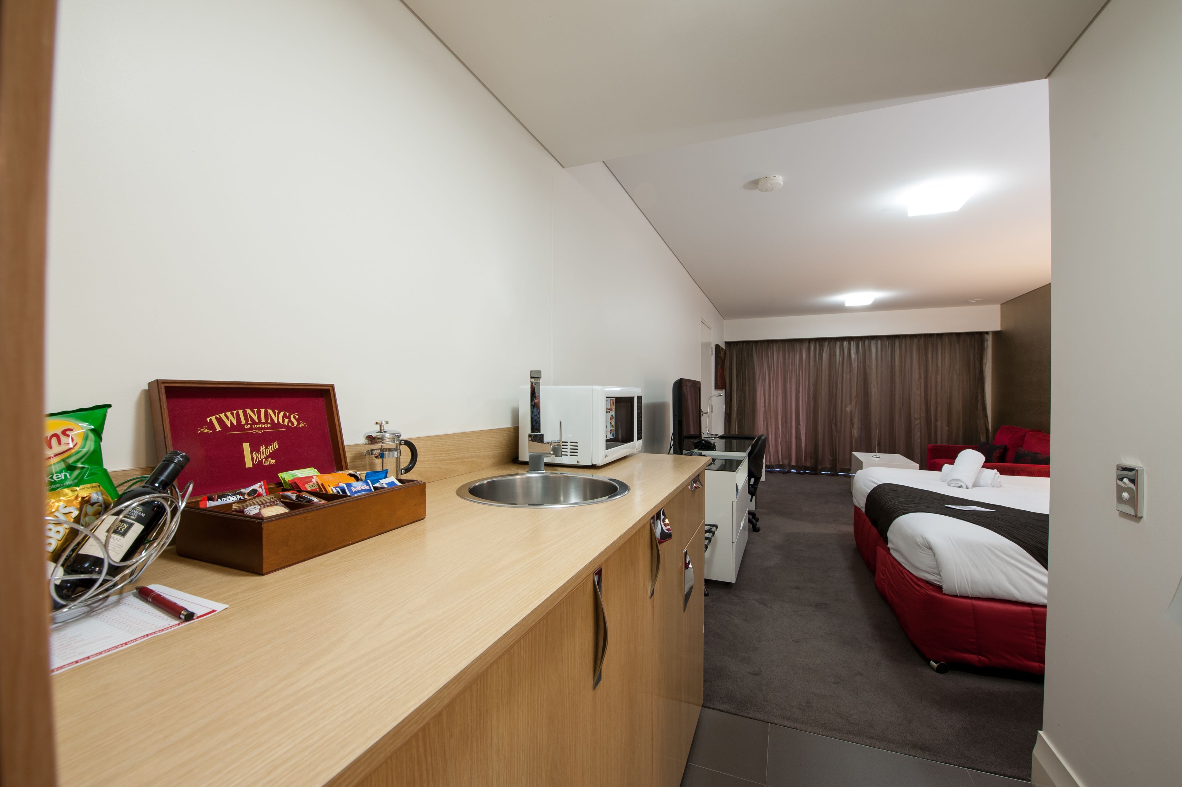 A hotel room with a kitchenette, a bed, and a bathroom.