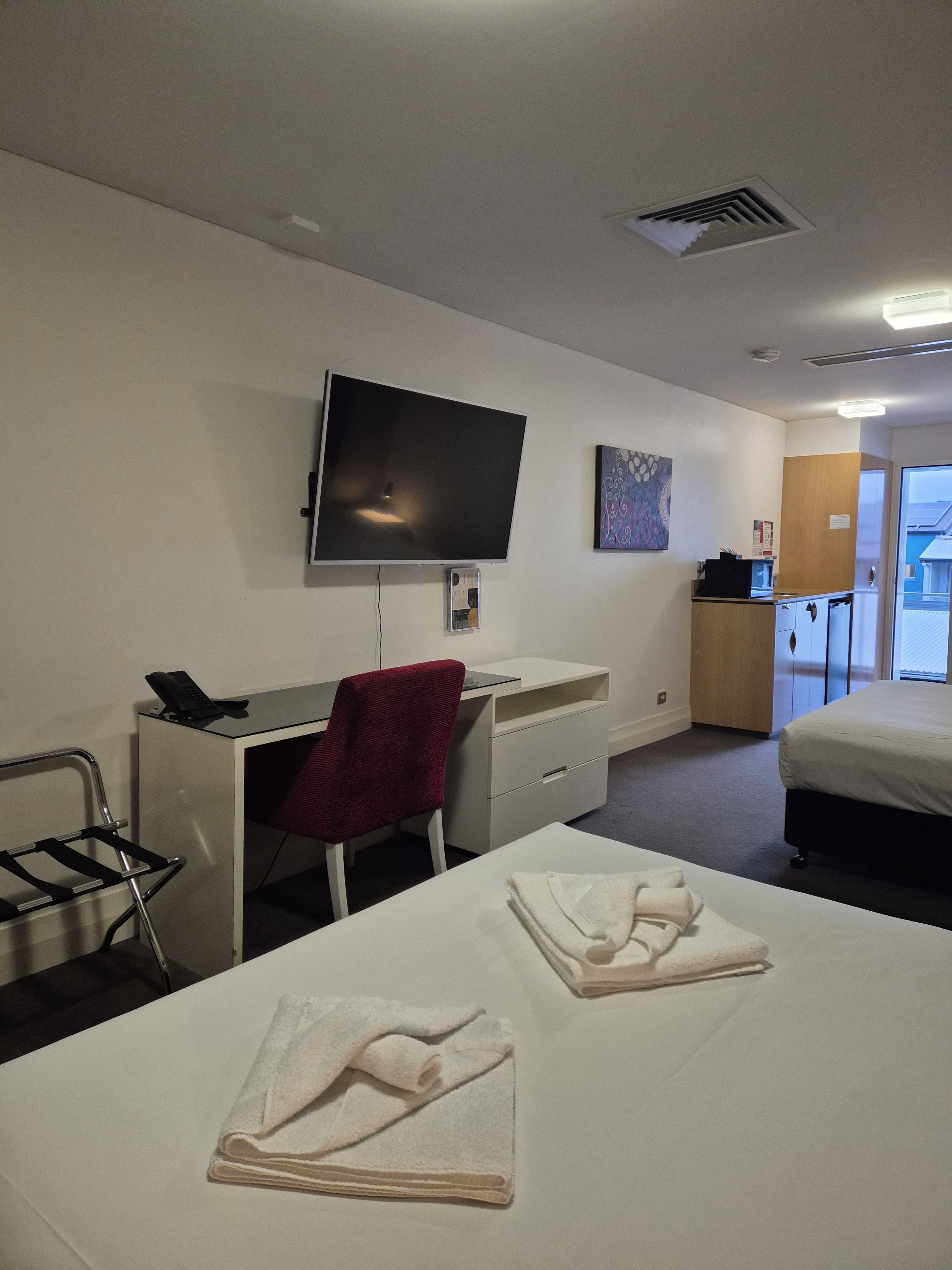 A hotel room with a bed, a desk with a chair, a television, and a small kitchenette.