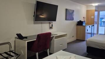 A hotel room with a bed, a desk with a chair, a television, and a small kitchenette.