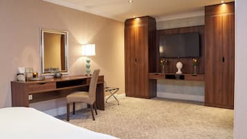 A hotel room with a bed, a desk with a chair, a large mirror, a flat-screen TV, and wooden wardrobes.