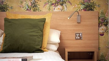 Een net opgemaakt bed met een groen en geel kussen, een wit kussen en een boek getiteld "Rae Morris" op het nachtkastje.