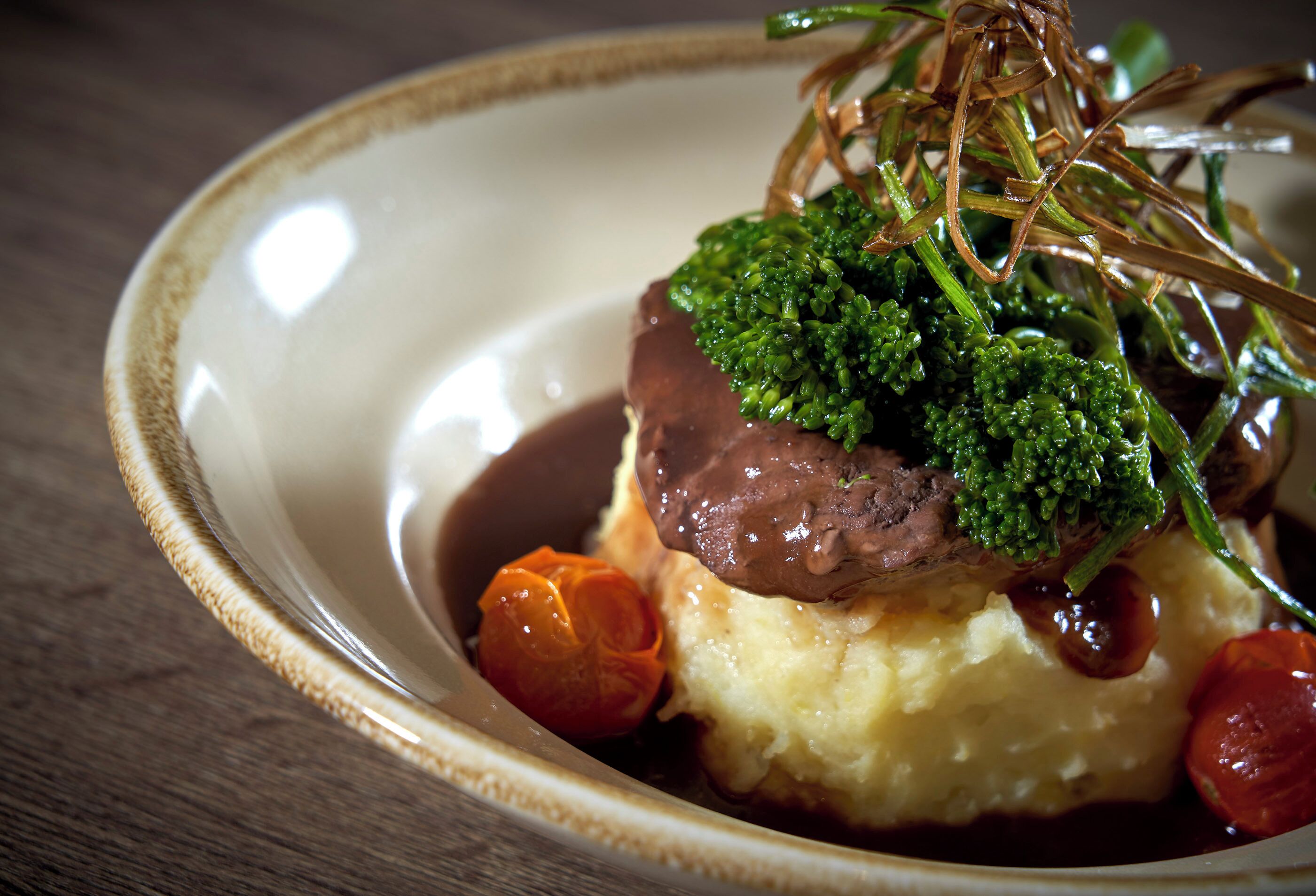 Une assiette contenant de la purée de pommes de terre, un morceau de viande, des brocolis et une petite tomate.