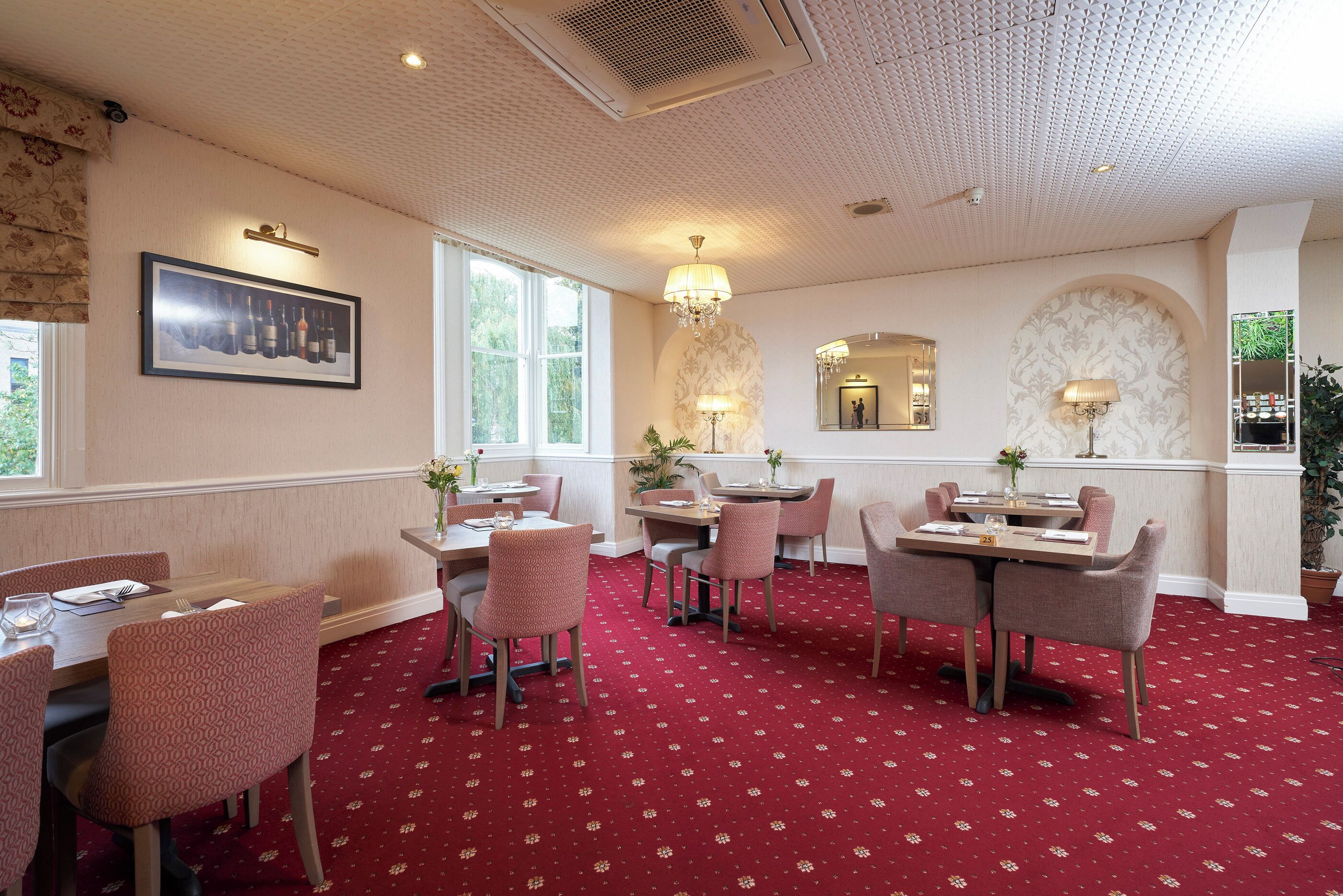 A dining area with red carpet flooring, wooden tables, and upholstered chairs.