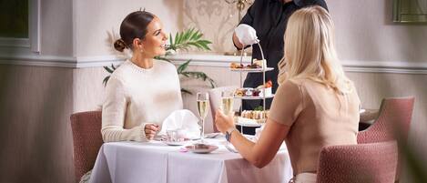 Une table à manger recouverte d’une nappe blanche, deux chaises et un chariot à desserts.