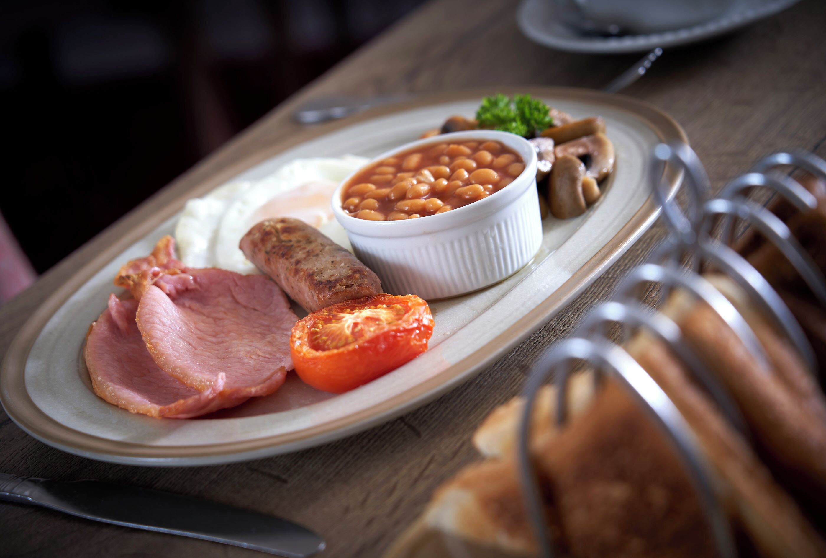 Un plato con frijoles, jamón, tomate y champiñones.