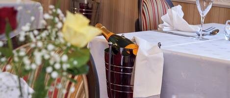 A dining table with a bottle of champagne in a metal bucket, a glass of water, and a vase with flowers.