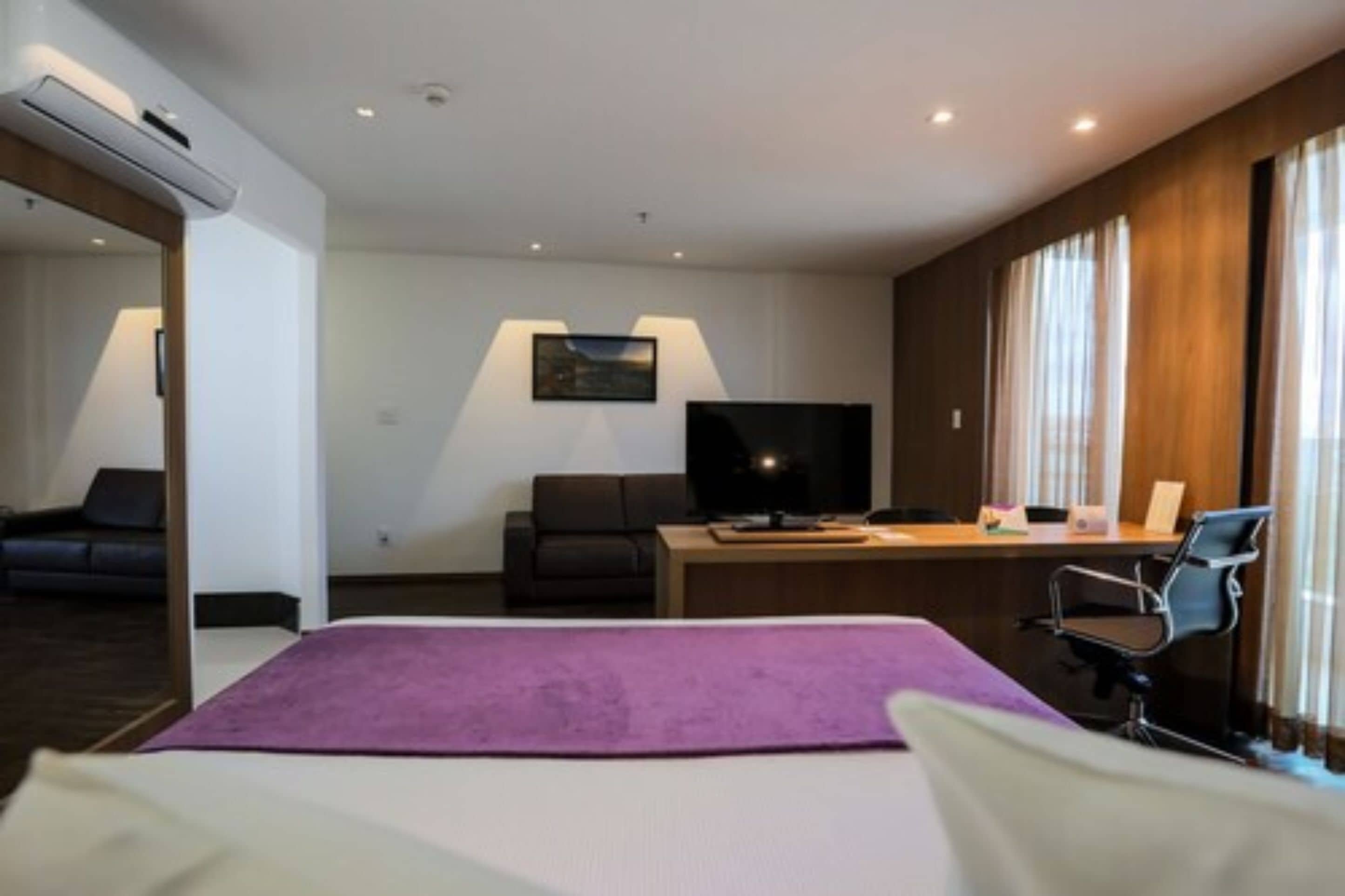 Una habitación de hotel con cama, escritorio, computadora, televisor y una silla.