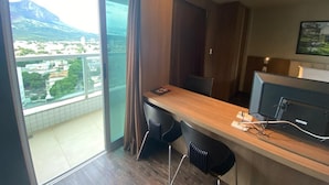 A modern hotel room with a balcony, a wooden desk, two black chairs, and a television.