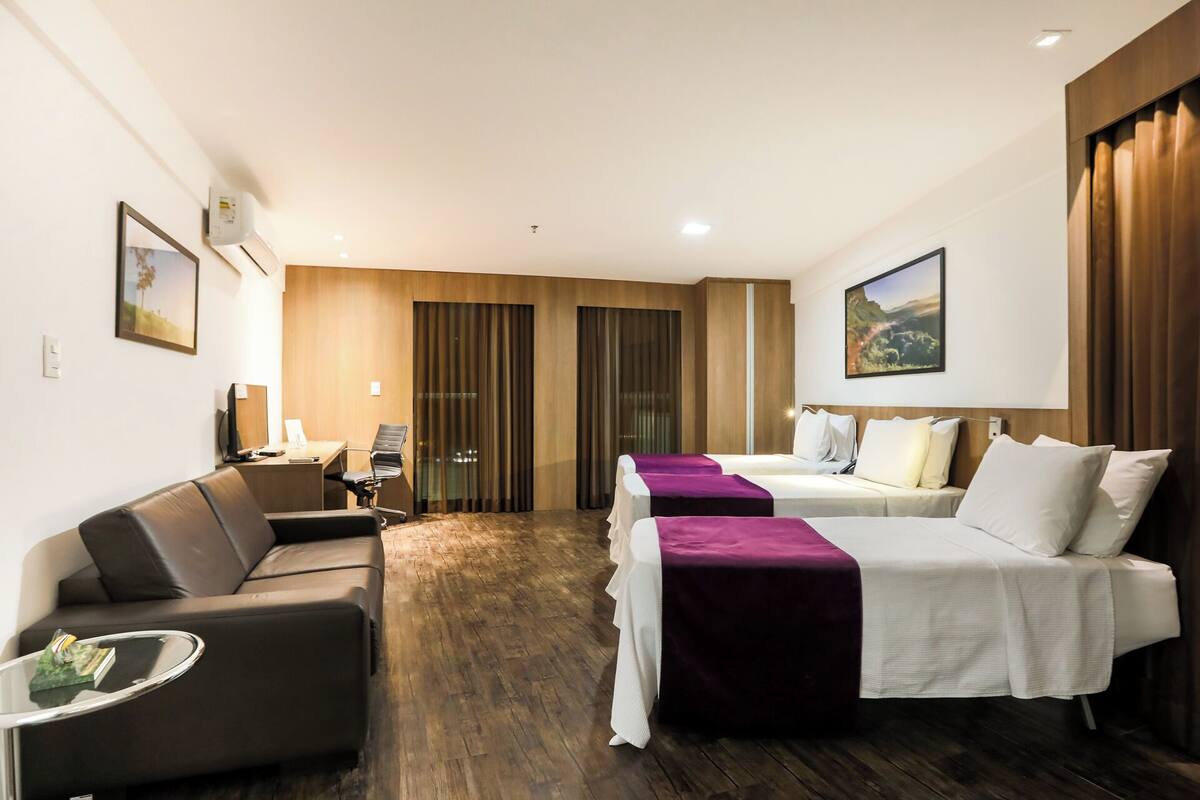 Habitación de hotel con dos camas, un sofá, un escritorio y un televisor.