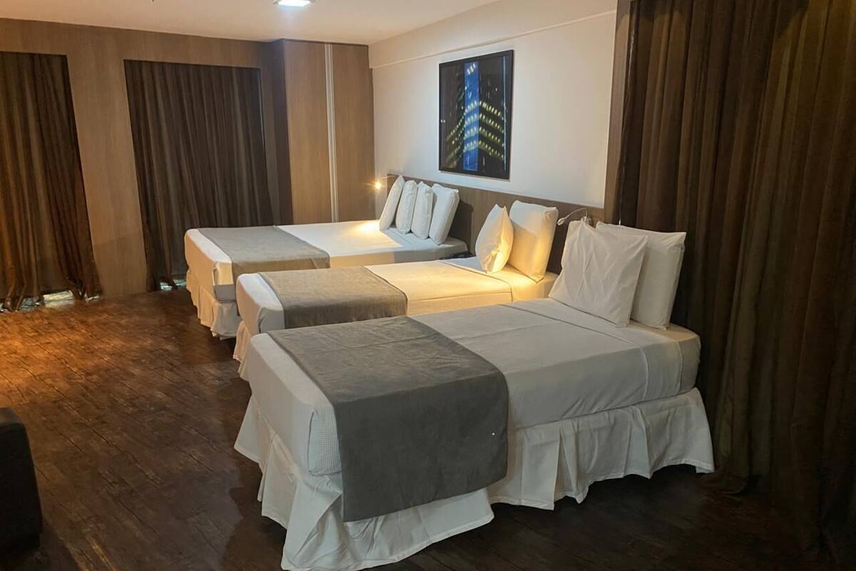 Habitación de hotel con dos camas, un ventanal grande y vistas a la ciudad.