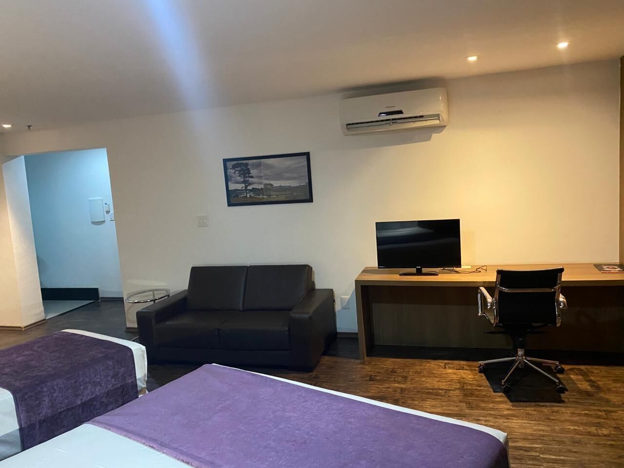 Habitación de hotel con dos camas, un sofá, un escritorio con computadora y un equipo de aire acondicionado.