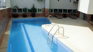 A swimming pool with a metal ladder, potted plants, and lounge chairs.