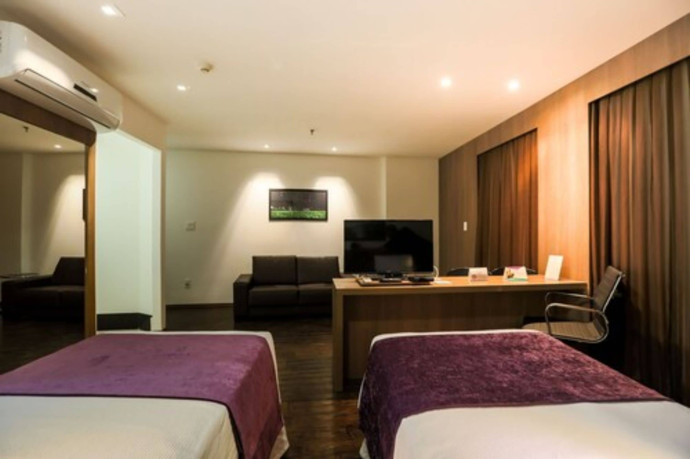 A hotel room with two beds, a desk with a chair, a television, and a wall-mounted artwork.