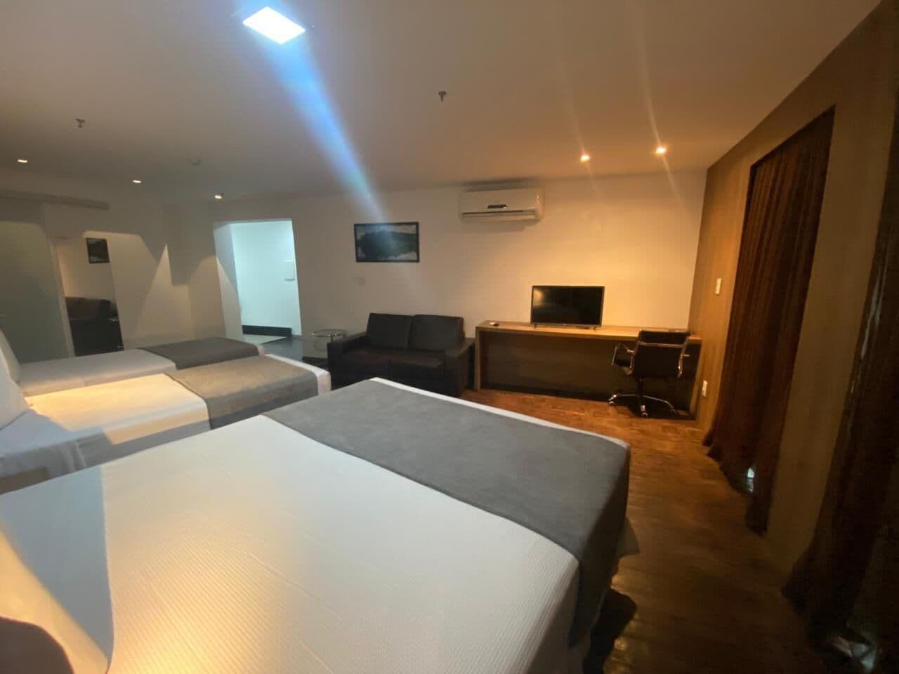 A hotel room with two beds, a sofa, a desk, and a television.