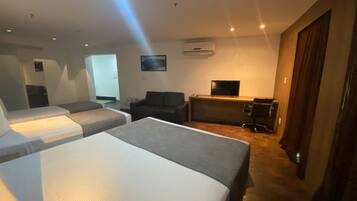 A hotel room with two beds, a sofa, a desk, and a television.