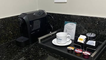 Una estación de café con cafetera, una taza y sobrecitos de azúcar sobre una bandeja.