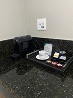 Una estación de café con cafetera, una taza y sobrecitos de azúcar sobre una bandeja.