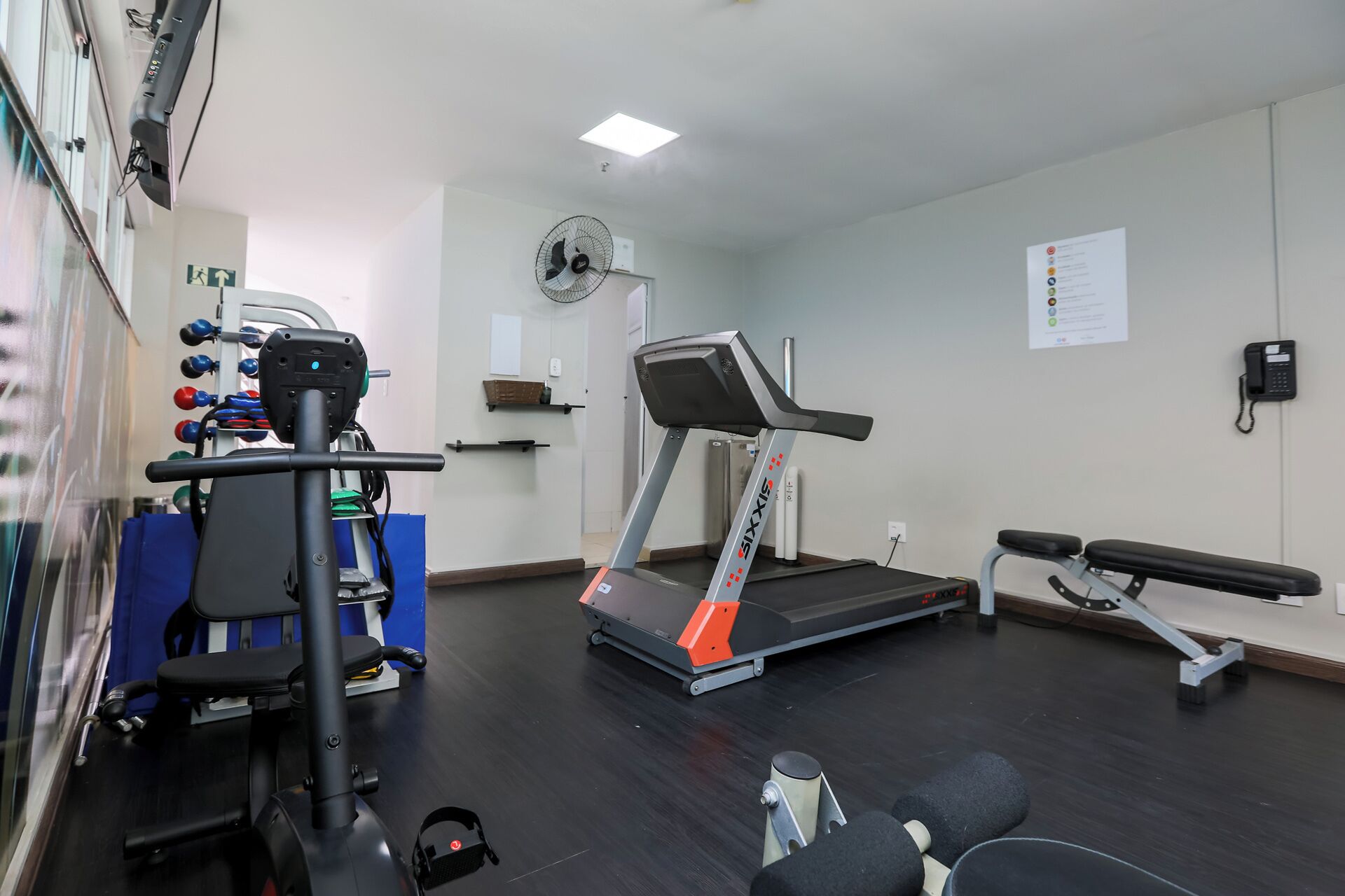 A gym with a treadmill, weight machines, a bench, and a fan.