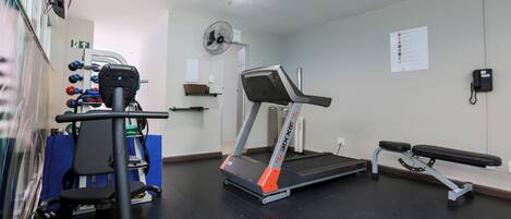 A gym with a treadmill, weight machines, a bench, and a fan.