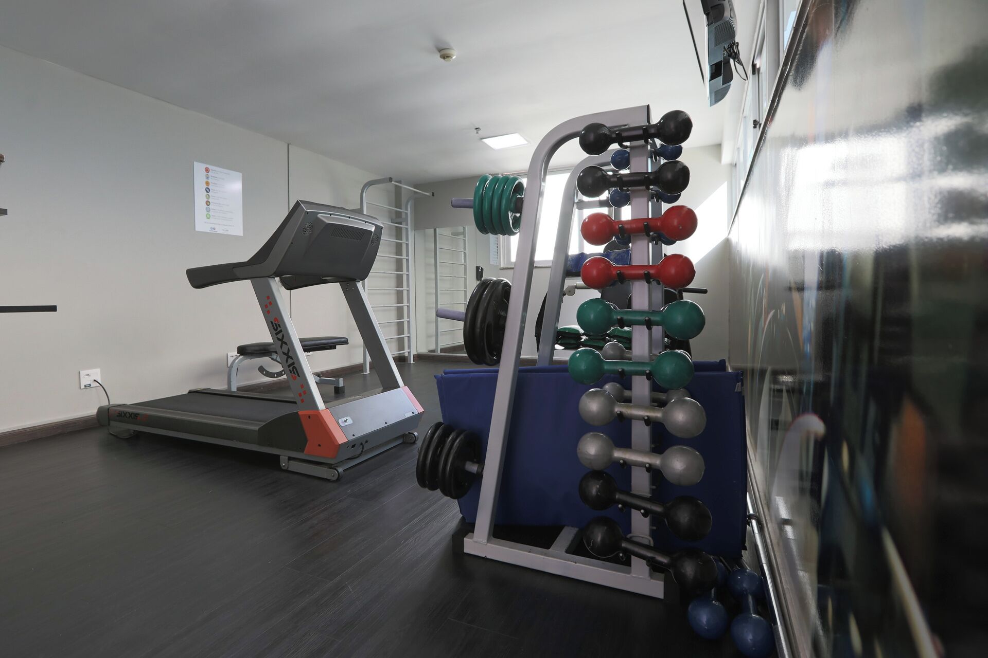 A gym with a treadmill, weightlifting equipment, and a bench.