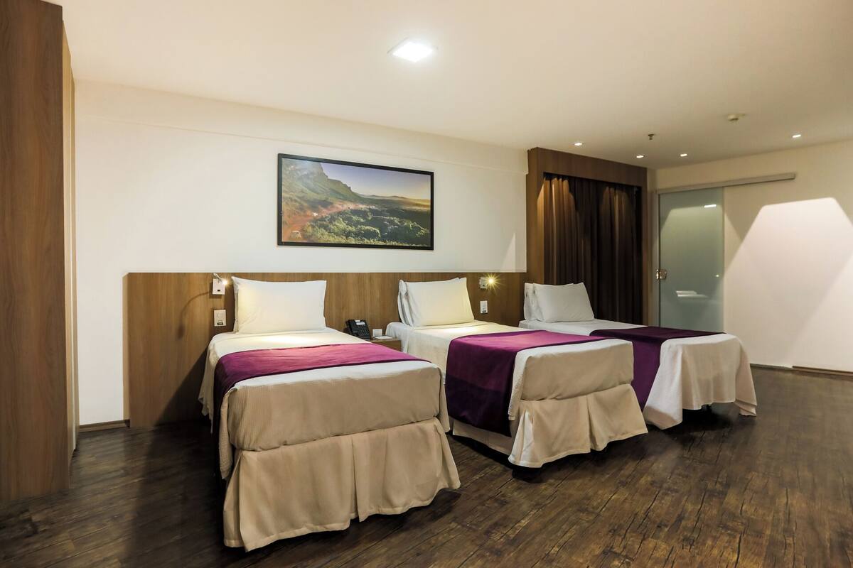 Habitación de hotel con dos camas, un cuadro en la pared y una puerta corrediza de vidrio.