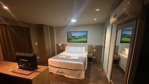 A hotel room with a large bed, a desk with a computer, and a TV mounted on the wall.