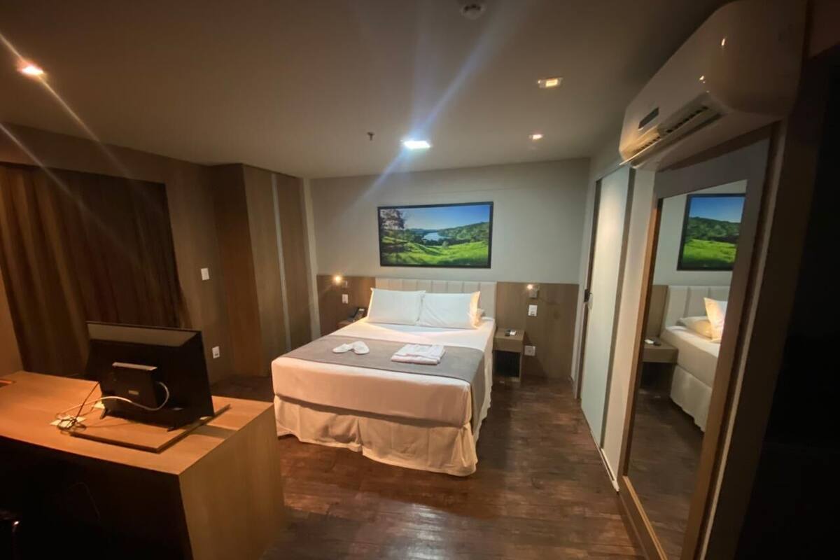 Una habitación de hotel con una cama grande, un escritorio con computadora y un televisor montado en la pared.