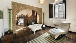 Ein Badezimmer mit freistehender Badewanne, einem grün gestreiften Teppich und einem weißen Sessel.