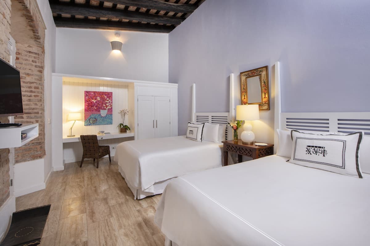 Habitació d'hotel amb dos llits, una escriptori, un televisor i una paret de maó.