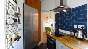 A modern kitchen with a stainless steel refrigerator, a wooden accent wall, and a blue-tiled backsplash. - Arthouse (Canterbury)
