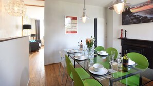 A dining area with a glass table, green chairs, and a painting on the wall. - Arthouse (Canterbury)