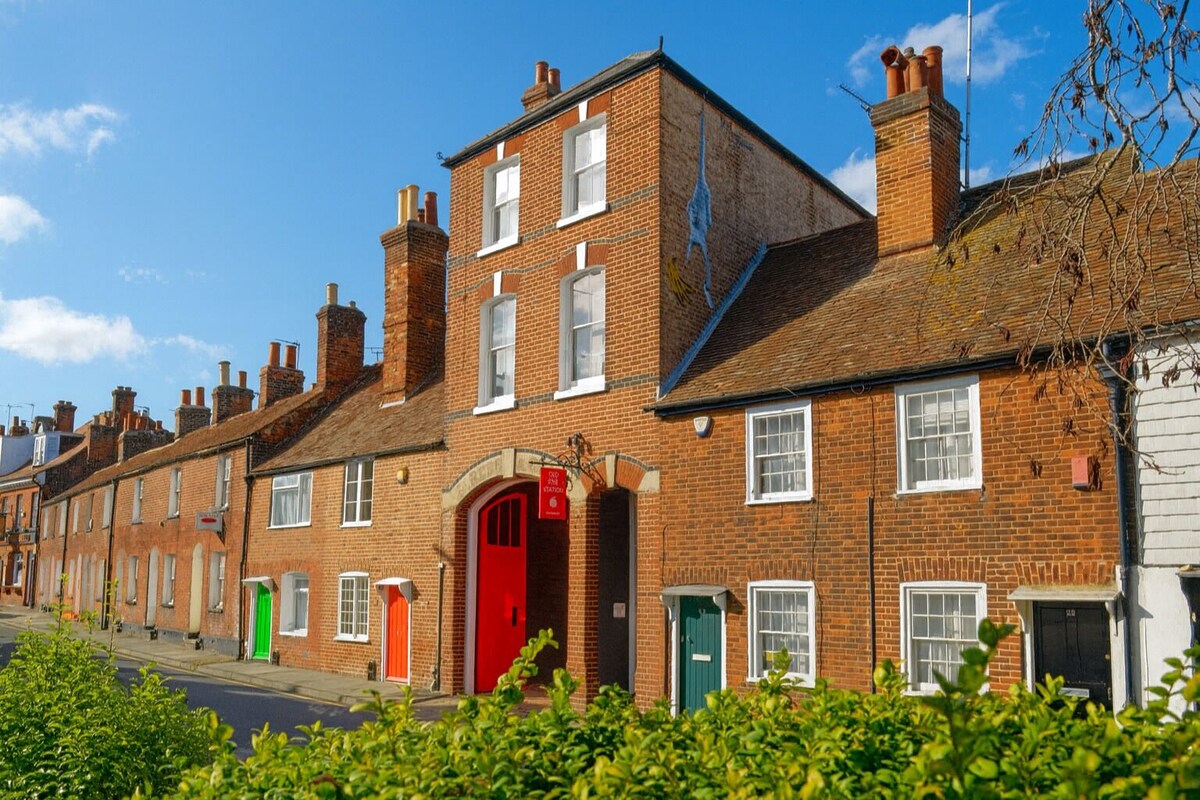A row of terraced houses with distinct red and green doors, brick facades, and a clear blue sky.