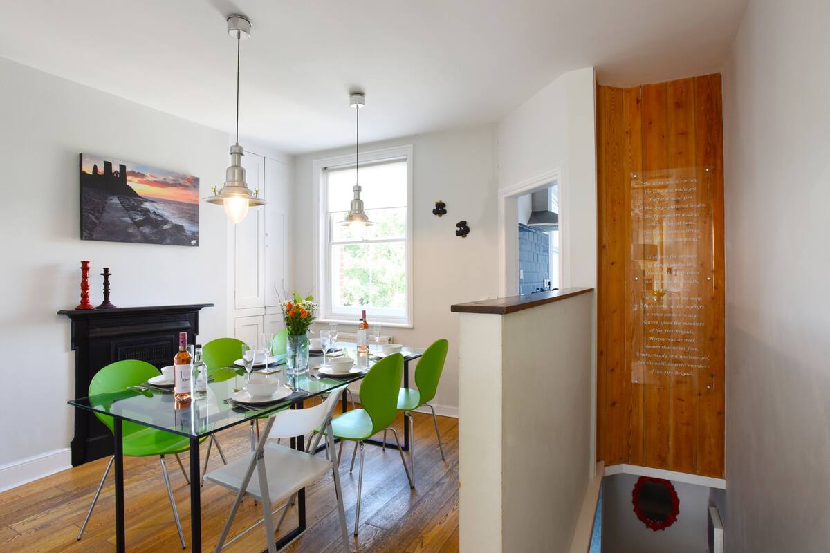 A dining area with a glass table, green chairs, and pendant lights.