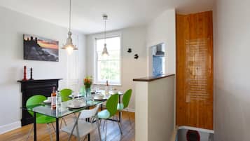 Un espace repas avec une table en verre, des chaises vertes et des luminaires suspendus.