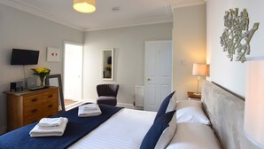 A hotel room with a bed, a dresser, a chair, a television, and a wall-mounted artwork. - Arthouse (Canterbury)