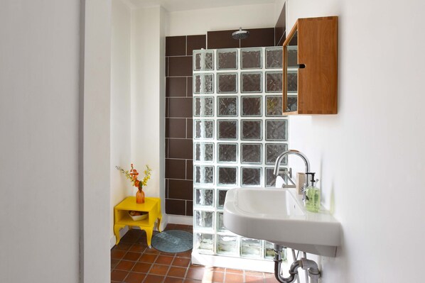A bathroom with a white sink, a yellow stool, and a glass shower enclosure. - Arthouse (Canterbury)