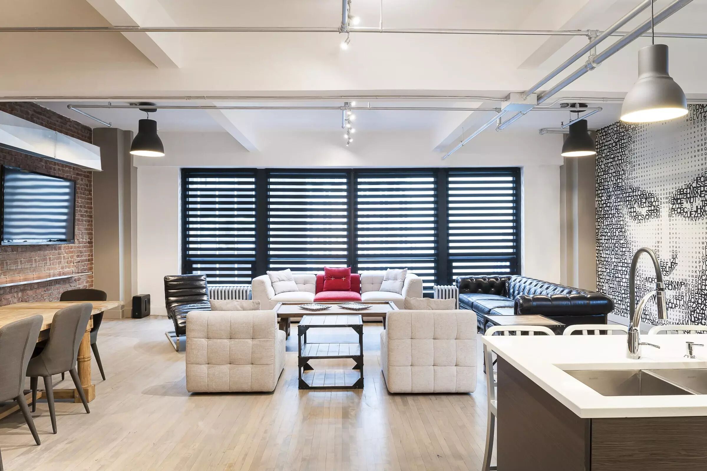 Eine moderne Küche mit einer zentralen Kochinsel, einem Essbereich mit Holztisch und -stühlen sowie einer Sitzecke mit Sofas und einem roten Akzentkissen.