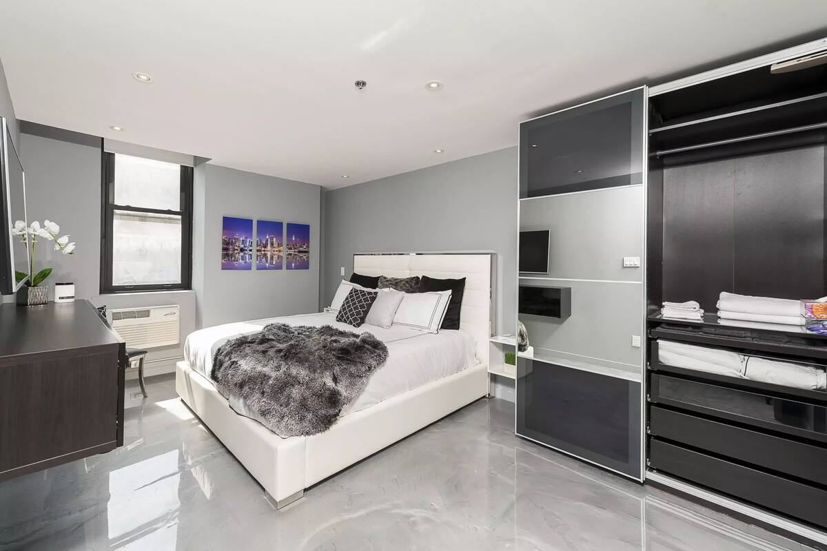 A modern bedroom with a large bed, a desk, and a walk-in closet.