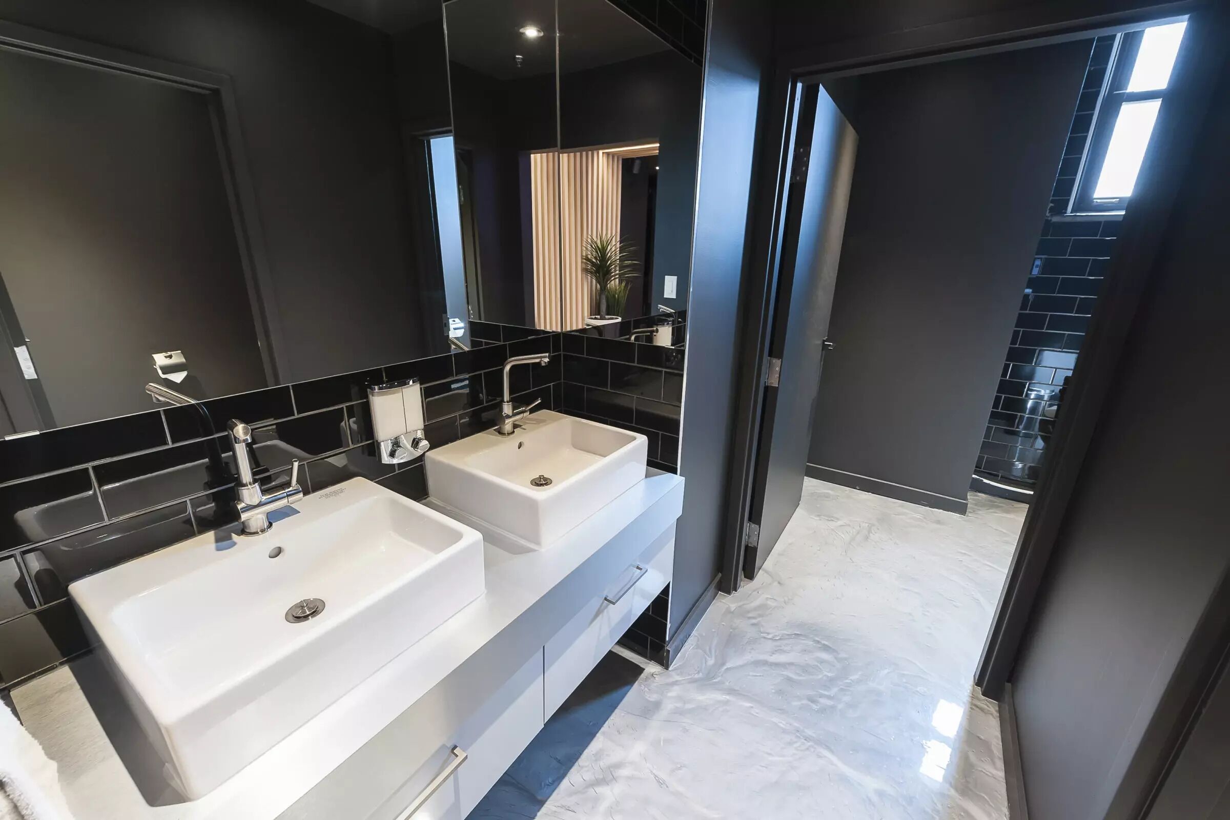 Une salle de bain moderne avec deux lavabos, un grand miroir et une vue sur la cuisine.