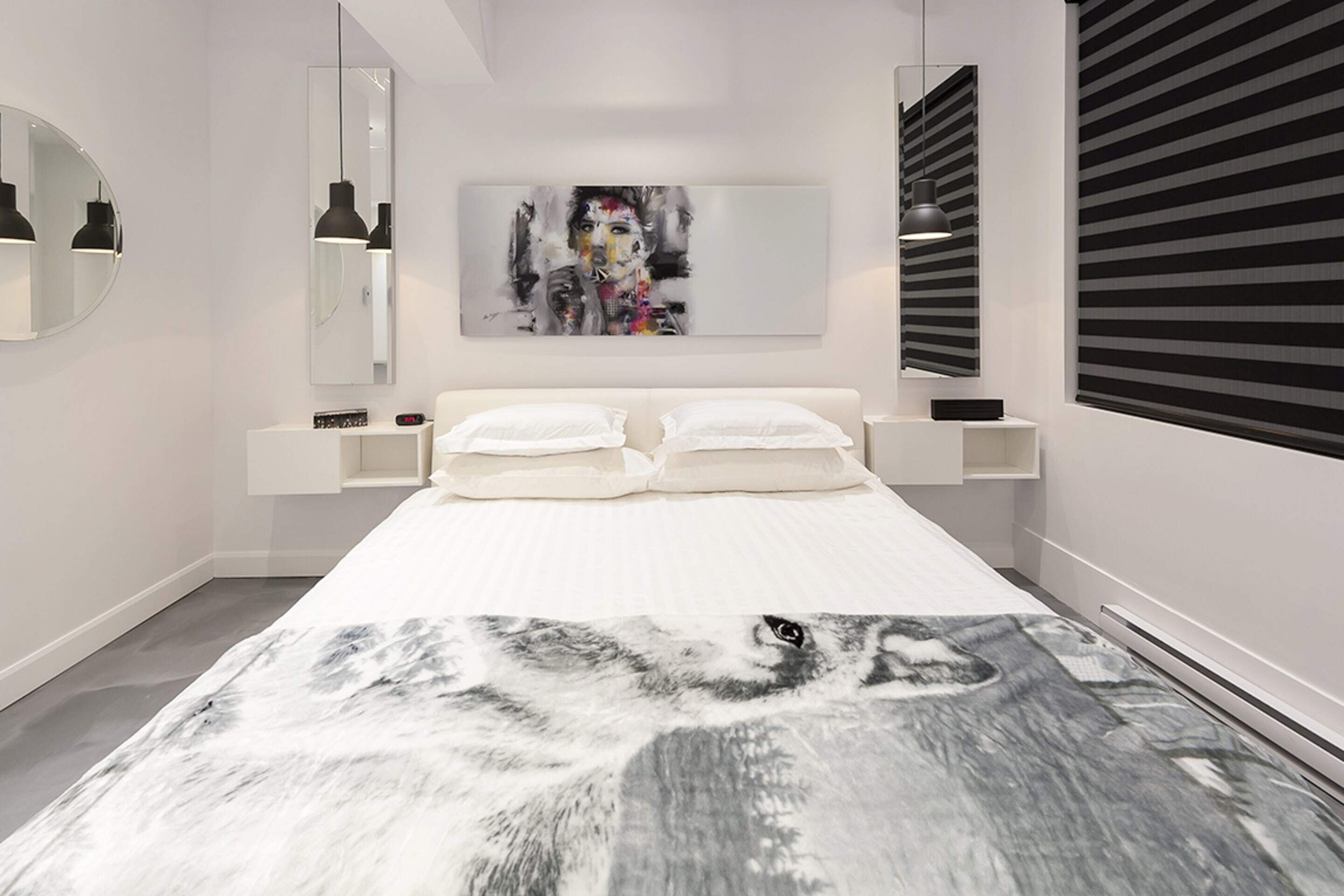 Une chambre moderne avec un grand lit, un miroir fixé au mur, un tableau et une fenêtre avec des stores.