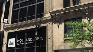 Un grand immeuble sur lequel on peut lire l’inscription « HOLLANDLOFTS par Simplissimmo.ca ».