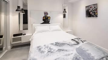 Une chambre à coucher moderne avec un grand lit, une tête de lit décorée d’œuvres d’art, des lampes de chevet et une armoire.