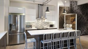 Une cuisine moderne dotée d’appareils électroménagers en acier inoxydable, d’un îlot central avec des tabourets de bar et d’un mur décoratif en briques.