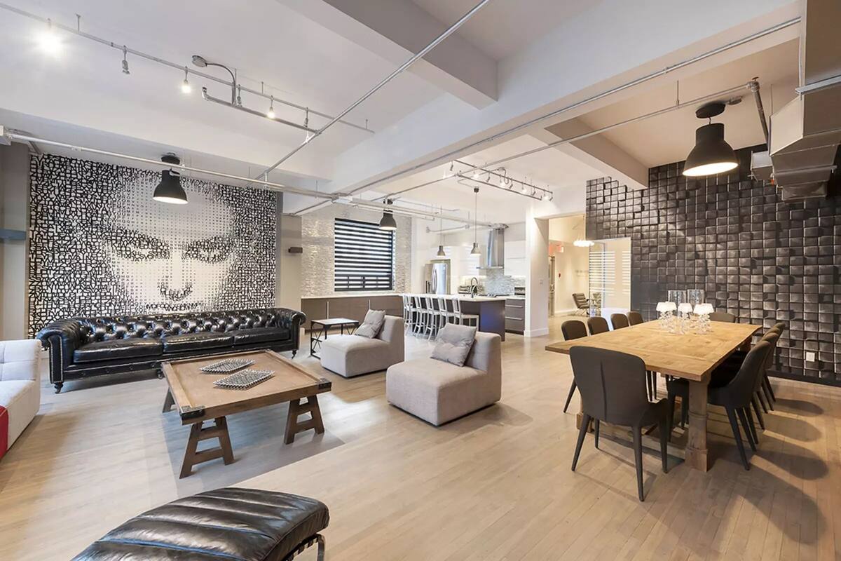 A spacious living area with a black leather sofa, a wooden coffee table, and a dining table with chairs. There is a kitchen in the background with a modern design.