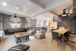 A spacious living area with a black leather sofa, a wooden coffee table, and a dining table with chairs. There is a kitchen in the background with a modern design.