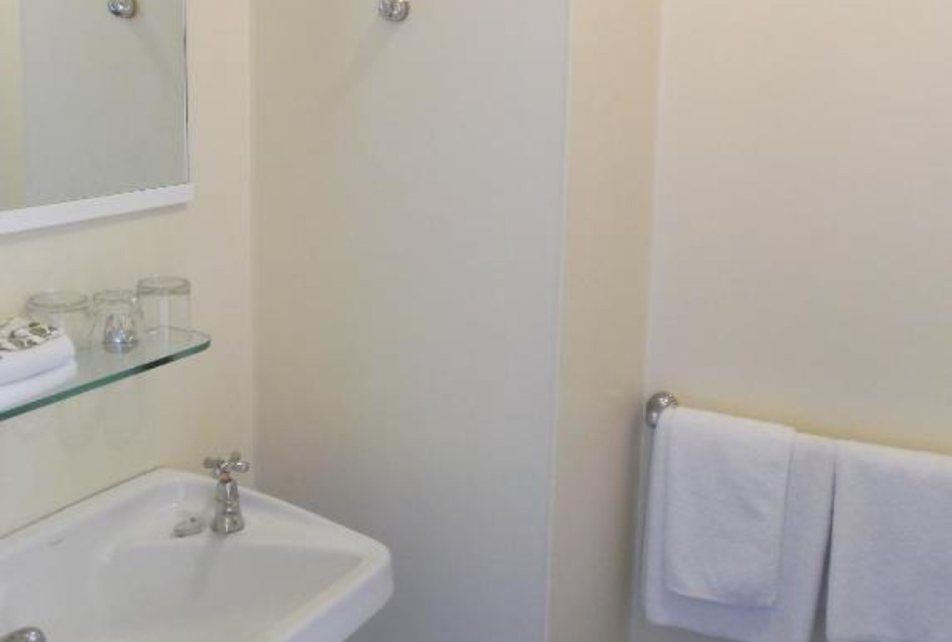 A bathroom with a white sink, a glass shelf above it, and a towel hanging on a towel rack.