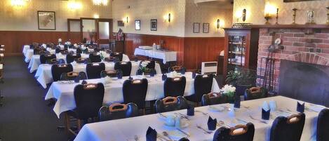 A banquet hall with rows of tables set for dining, chandeliers, and a fireplace.