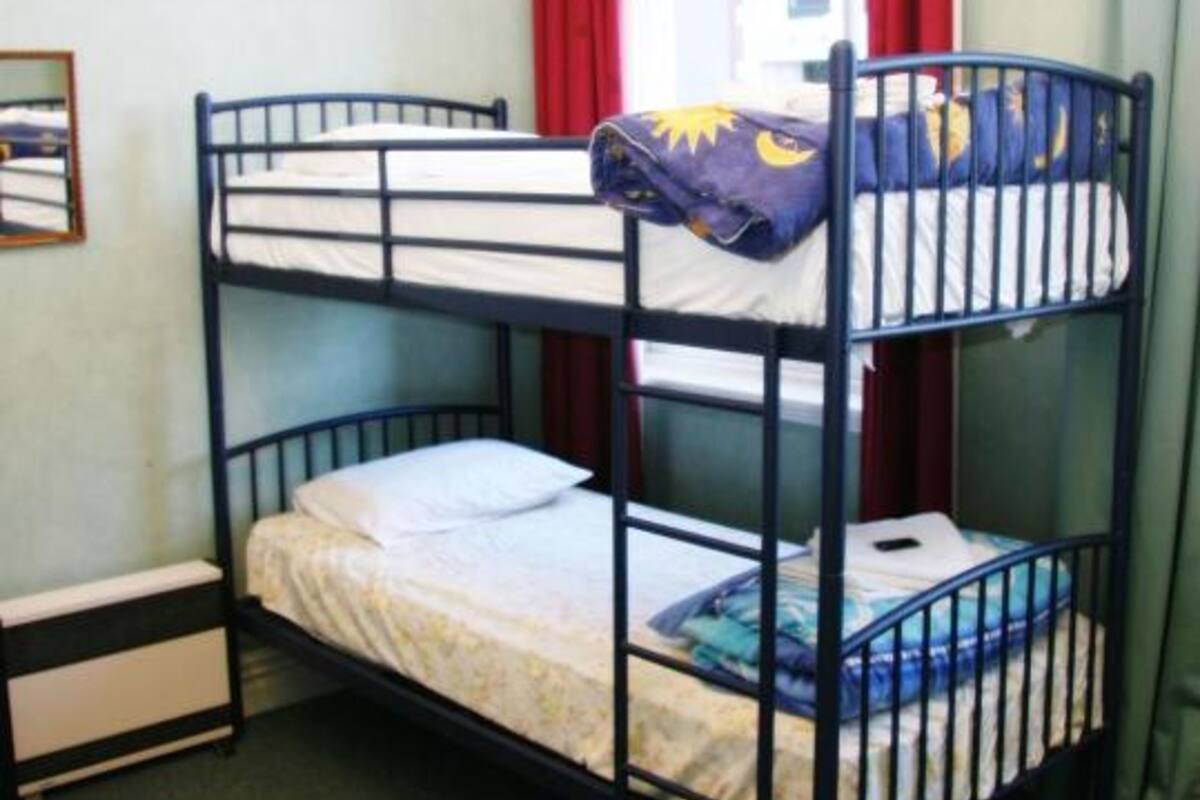 A bunk bed with two levels, a small bedside table, and a window with red curtains.
