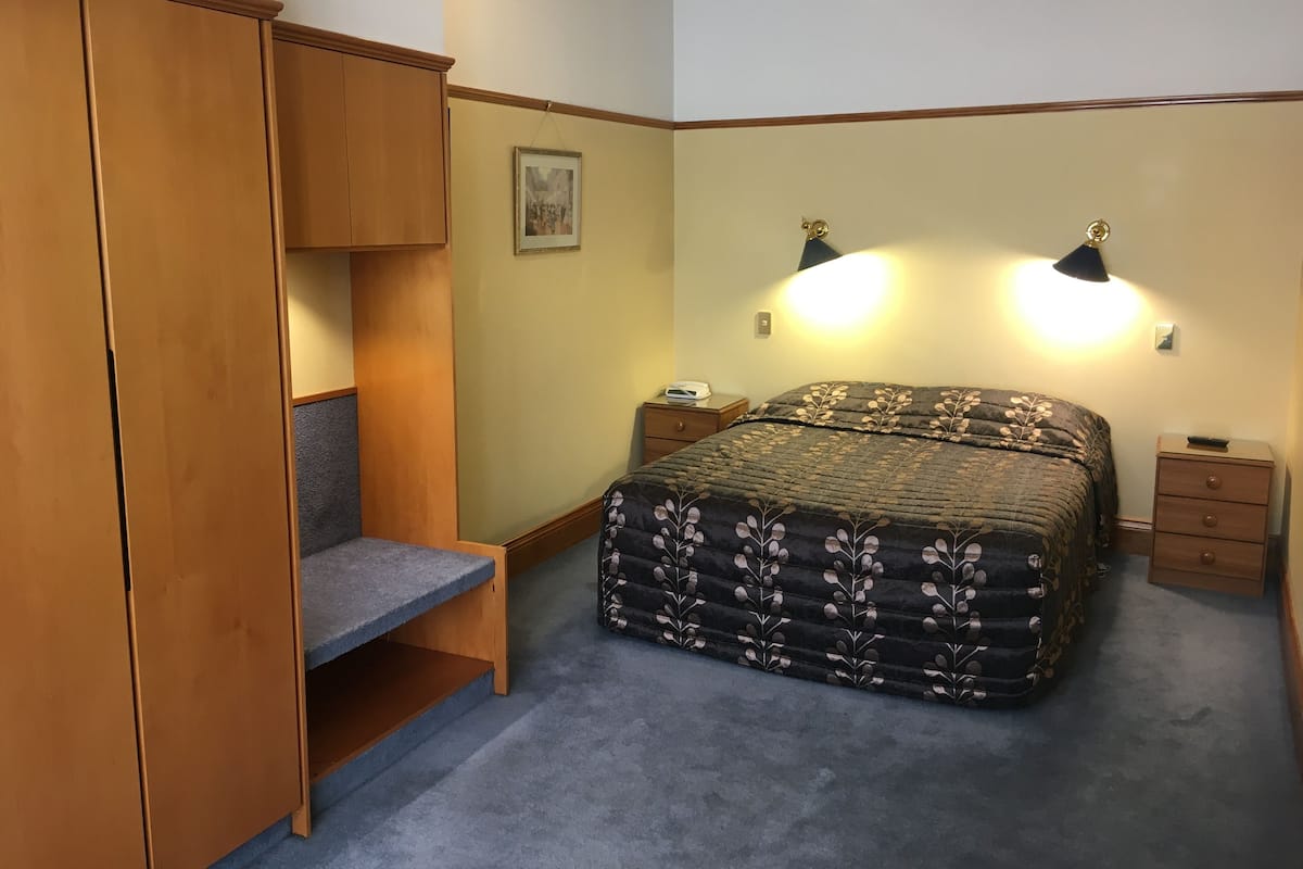 A bedroom with a bed, a wardrobe, a desk, and two bedside lamps.